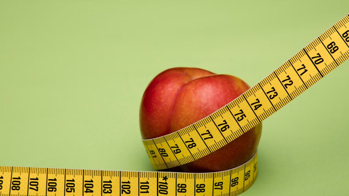 Red apple wrapped in a yellow measuring tape against a green backdrop emphasizes freshness and health.