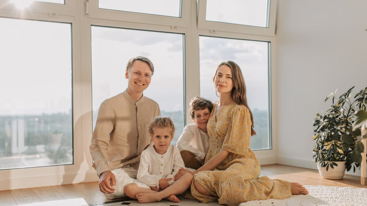 A cheerful family of four sitting together on the floor of a sunlit living room.
